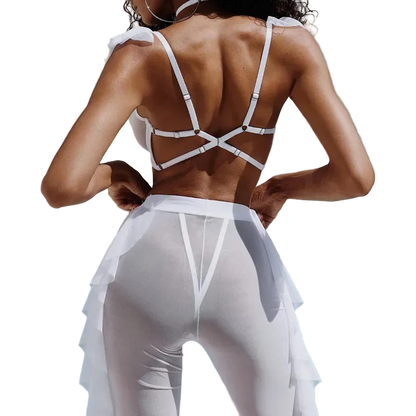 A woman shown from behind wearing a white strappy bikini top and matching white ruffled swim cover-up bottoms, standing by a swimming pool.