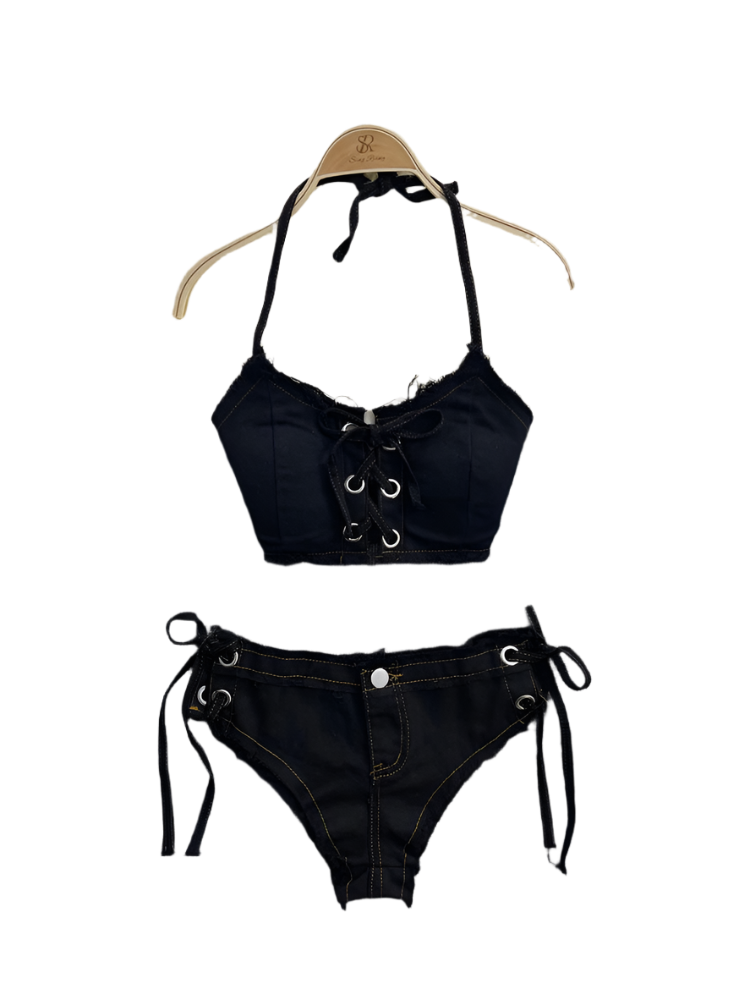Black lace-up bikini set on a gray surface with a fluffy white rug and pearl necklace in the background.