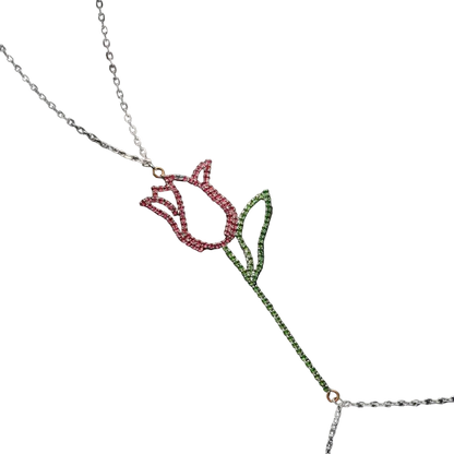 A silver-toned lariat necklace featuring a tulip pendant with a pink rhinestone flower head and a green rhinestone stem and leaves, displayed on a dark textured background.