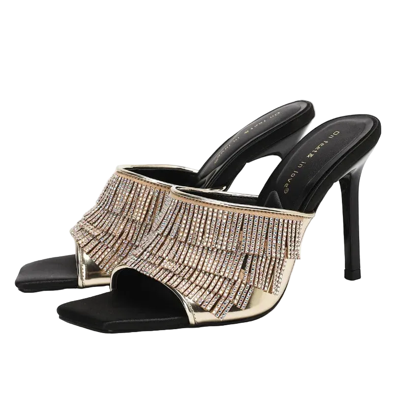 A pair of black open-toe high-heeled mule sandals with wide straps covered in cascading rhinestone fringe, shown on a clean white background.
