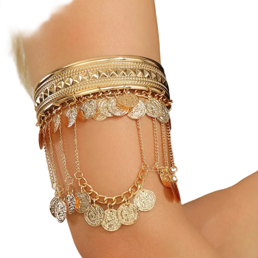 A close-up of a person's forearm wearing a layered gold bangle set with dangling coin and leaf charms, paired with a black satin sleeve.