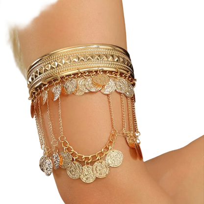 A close-up of a person's forearm wearing a layered gold bangle set with dangling coin and leaf charms, paired with a black satin sleeve.