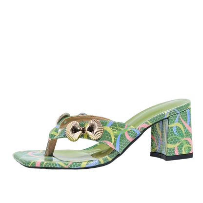 A green patterned thong sandal with a block heel, featuring a metallic gold shell-shaped ornament on the strap, shown against a plain white background.
