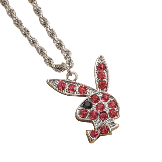 A silver bunny pendant necklace paved with red gemstones, featuring a small black gemstone for the eye, resting on a textured beige fabric background.