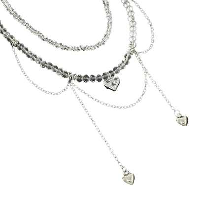 A layered silver necklace set featuring a beaded top layer, delicate chain dangles, and three small heart charms, displayed on a black background.