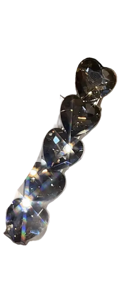 A set of five heart-shaped clear rhinestones attached to a white display card, held by a hand with glittery nail polish in a blurred indoor setting.