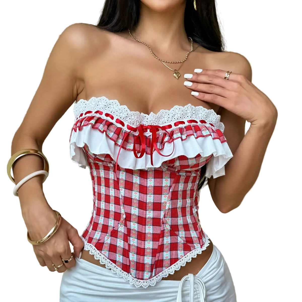 A woman wearing a red and white gingham strapless corset top with white lace ruffles and a red bow, paired with white bottoms, standing against a textured beige wall.