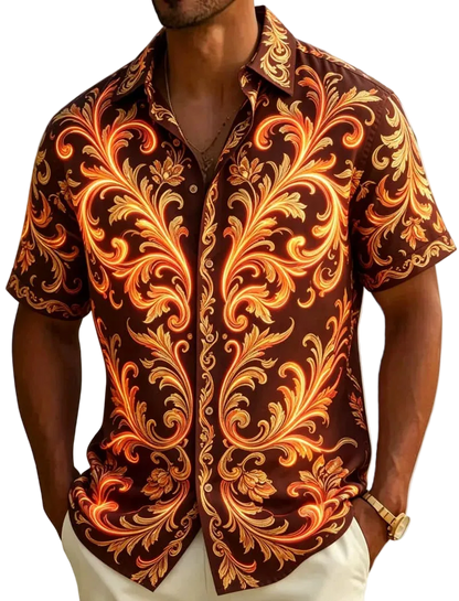 A man wearing a short-sleeve button-up shirt with an ornate baroque-style scroll pattern in orange, gold, and cream on a dark brown background, photographed outdoors near palm leaves and sand.