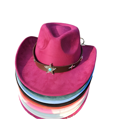 Stack of colorful cowboy hats with a purple top hat featuring a star and turquoise stone on grass.