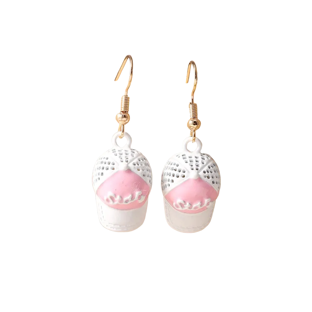 A pair of dangling earrings displayed on a beige jewelry stand. Each earring has a gold-tone fishhook wire and a white lace-like top section with a pink lower section shaped like a small cupcake or pastry.