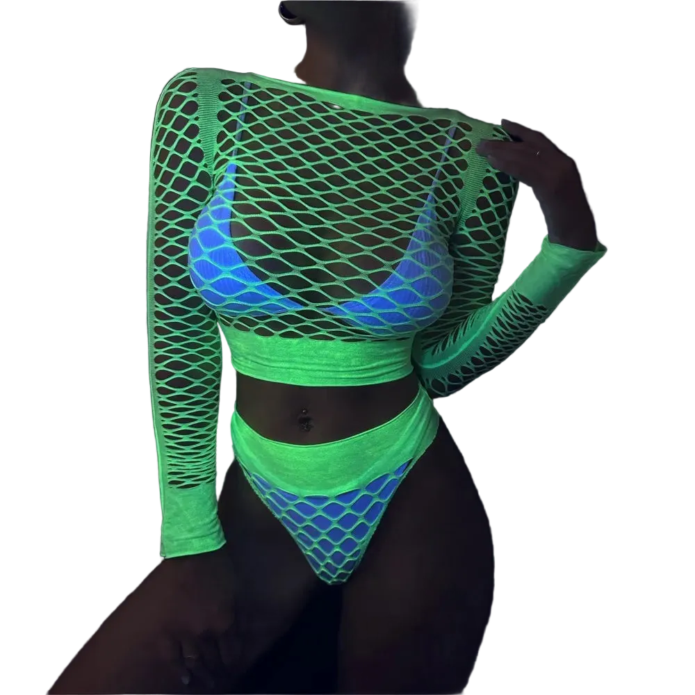 A model wearing a glowing neon green fishnet long-sleeve crop top and matching high-cut bikini bottoms with a blue and white patterned bralette underneath, photographed in a dark environment to show UV-reactive color.