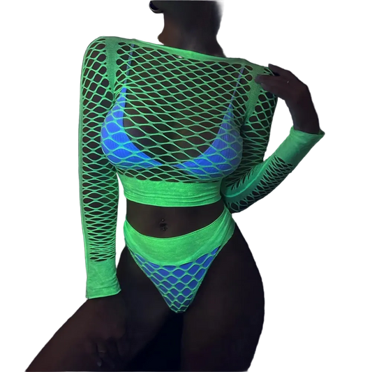 A model wearing a glowing neon green fishnet long-sleeve crop top and matching high-cut bikini bottoms with a blue and white patterned bralette underneath, photographed in a dark environment to show UV-reactive color.