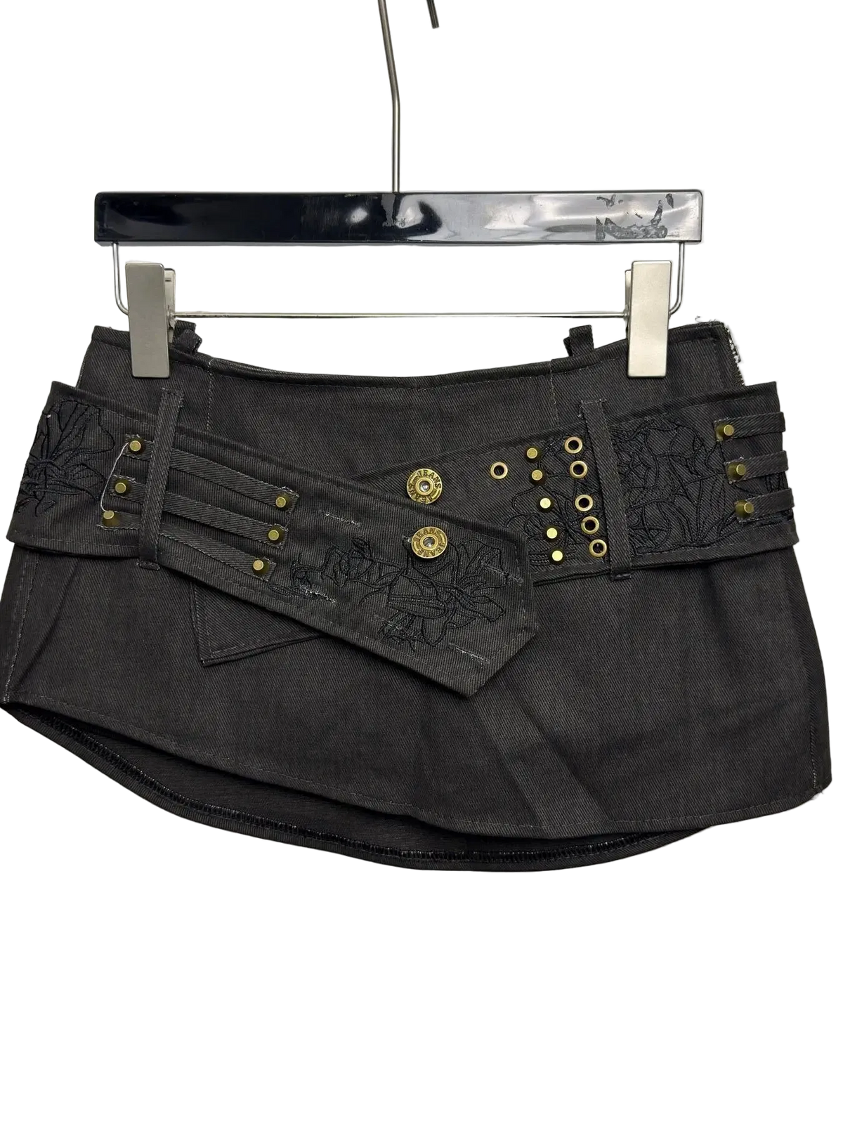A dark gray denim mini skirt with decorative gold-tone studs, grommets, and embroidered details, hanging on a black hanger against a plain light gray background.
