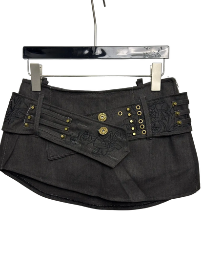A dark gray denim mini skirt with decorative gold-tone studs, grommets, and embroidered details, hanging on a black hanger against a plain light gray background.