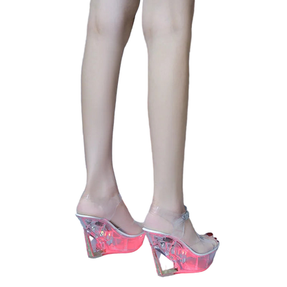 Clear high-heeled shoes worn by a person on a gray floor.