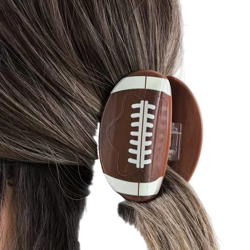 A football-shaped hair claw clip with a brown and white design, shown clipped to a person's dark hair.
