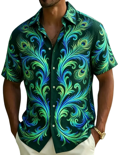 A man wearing a short-sleeve button-up shirt with a vibrant green, blue, and teal peacock feather pattern, photographed on a beach with palm leaves in the background.