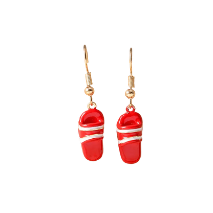 A pair of red and white slide-shaped drop earrings with gold hooks, displayed on a beige jewelry stand.