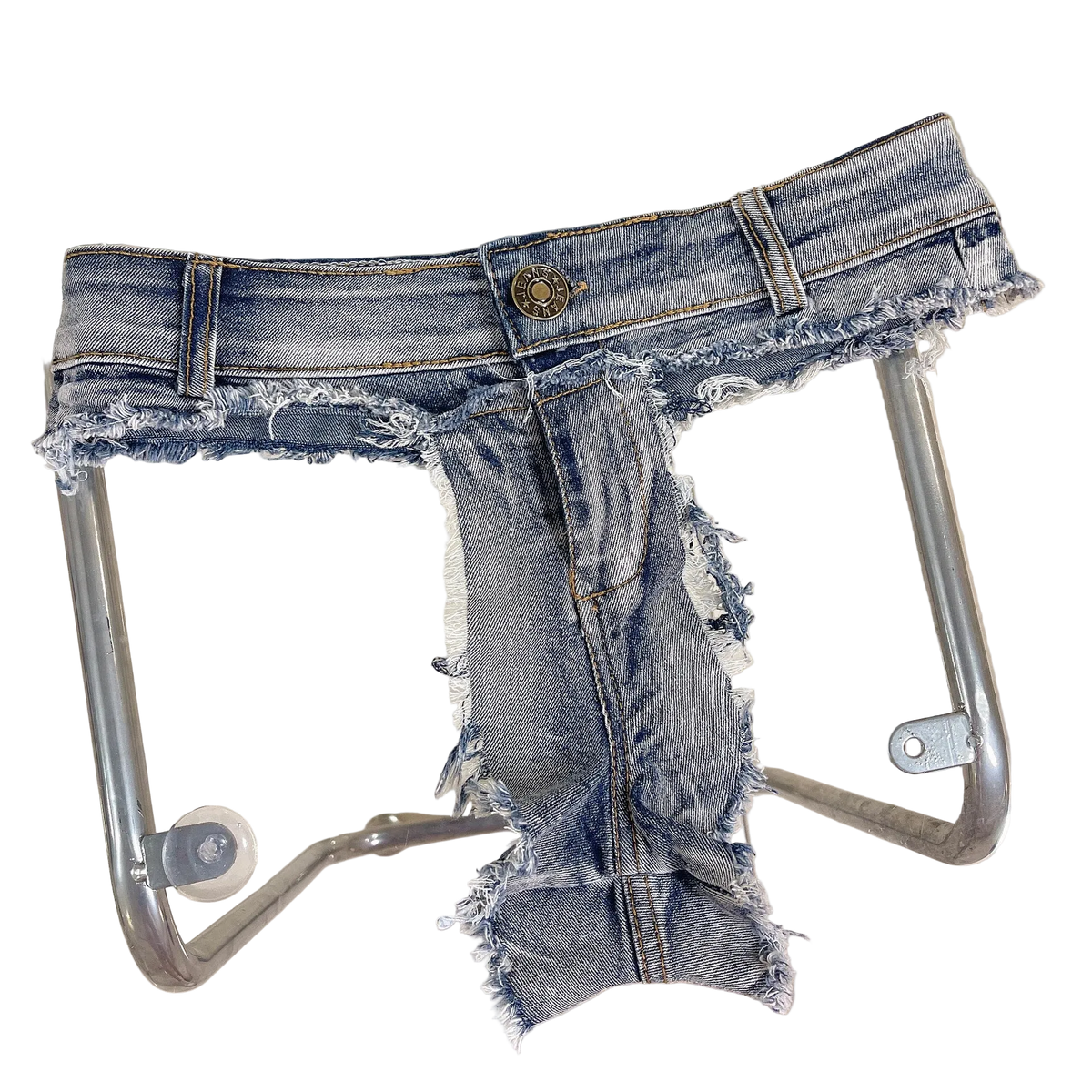 A pair of heavily distressed and ripped blue denim jeans with a frayed, raw hem and leg edges, displayed on a clear glass table with a metal frame.
