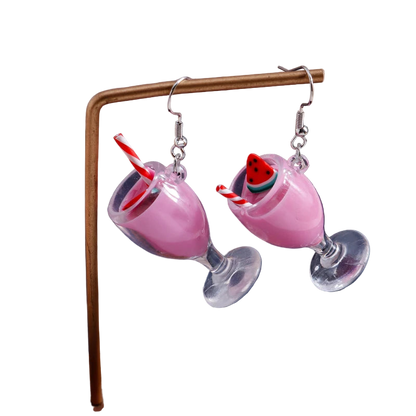 Pink cocktail glass earrings with a cherry on top on a stand against a dark background
