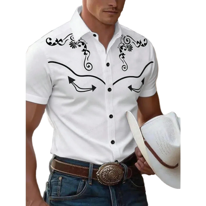 A man wearing a white short-sleeve western-style button-up shirt with black embroidered scrollwork and arrow details on the chest, paired with blue jeans and a brown belt, while holding a white cowboy hat.