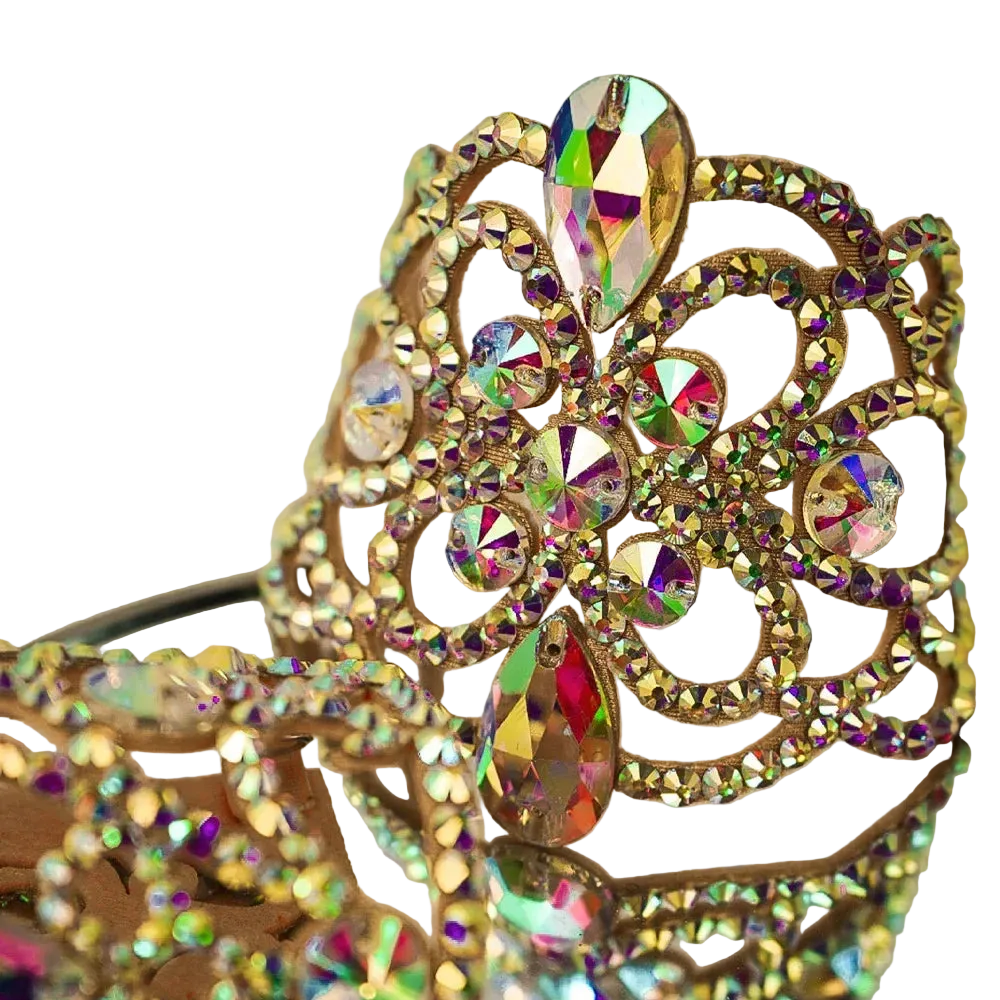 A close-up of an ornate gold crown embellished with iridescent rhinestones that reflect rainbow colors, set against a soft beige background.