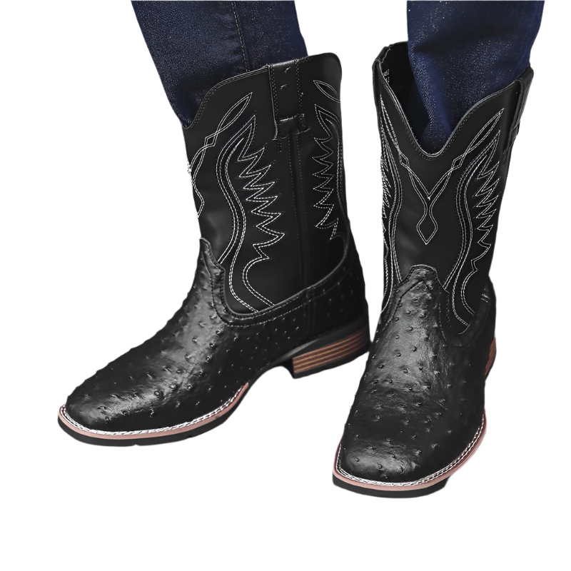 Black cowboy boots with white stitching on a wooden floor