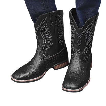 Black cowboy boots with white stitching on a wooden floor