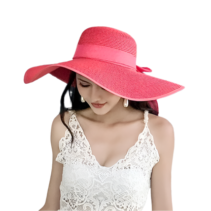 Woman wearing a large pink sun hat in front of a vintage vehicle.