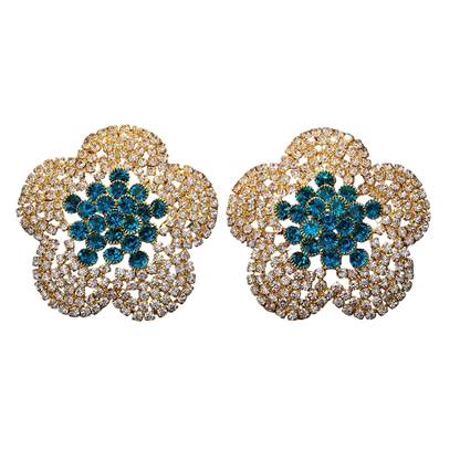 Pair of ornate earrings with blue center and gold and diamond-like border on black background