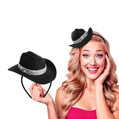 A smiling woman with long wavy blonde hair wears a small black hat with a sparkling silver band, while holding the same hat on a headband in her hand against a plain white background.