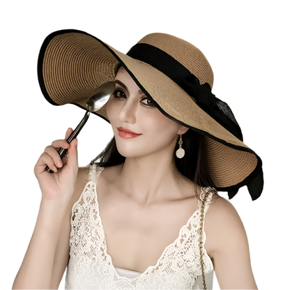 Woman wearing a large straw hat with a black ribbon, sitting in an outdoor setting.