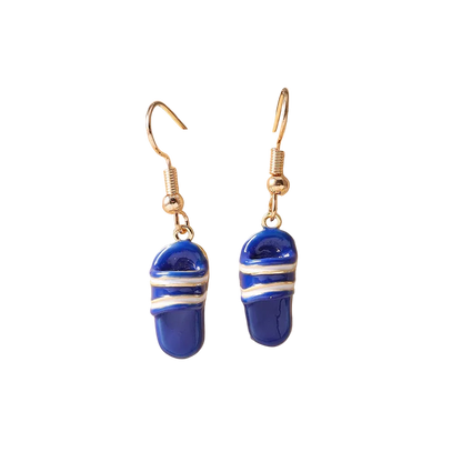A pair of dangling earrings with blue slipper-shaped charms wrapped in white stripes, hanging from gold-tone hooks on a beige ceramic display stand.