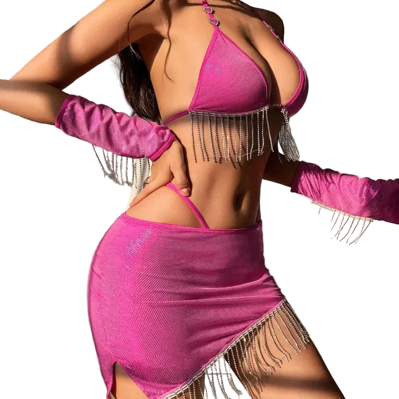 A woman wearing a bright pink fringed lingerie set with matching long gloves, posed in a bedroom setting with a bed visible in the background.