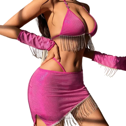 A woman wearing a bright pink fringed lingerie set with matching long gloves, posed in a bedroom setting with a bed visible in the background.
