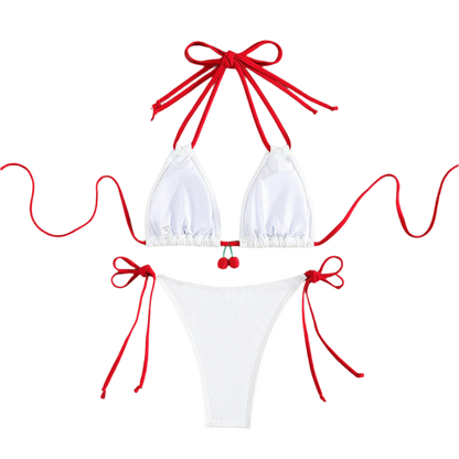 A white bikini with red string ties and cherry embellishments on the top. The design is simple yet charming, with a touch of whimsy.
