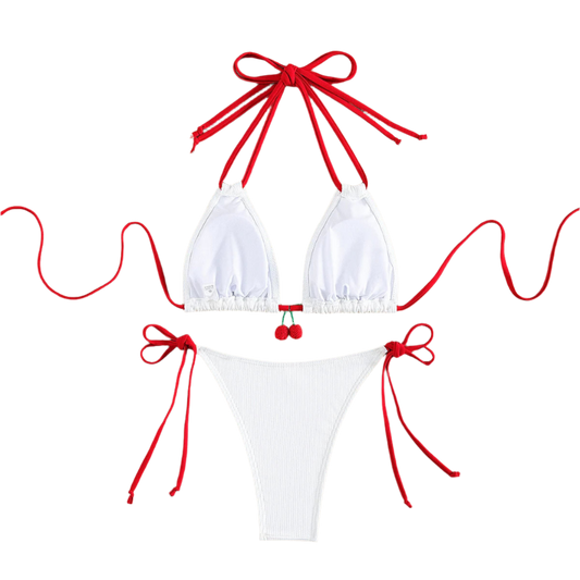 A white bikini with red string ties and cherry embellishments on the top. The design is simple yet charming, with a touch of whimsy.
