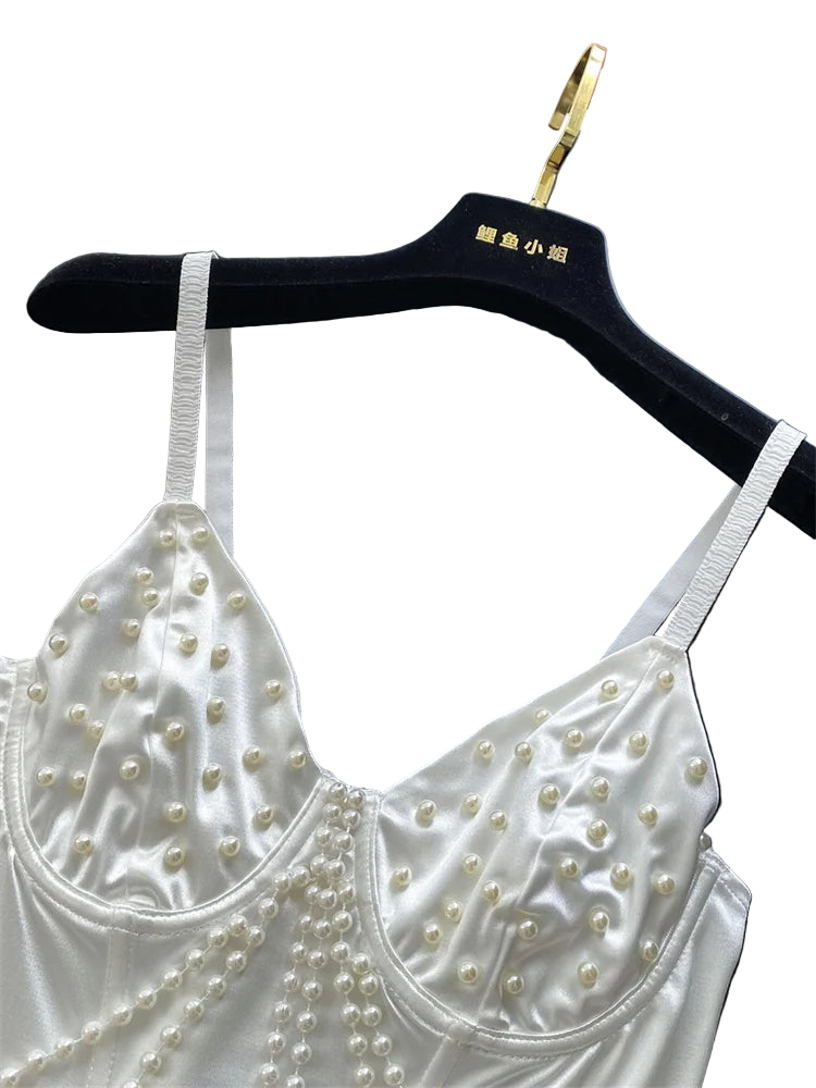 White lace top with pearl embellishments on a black hanger against a white curtain background.