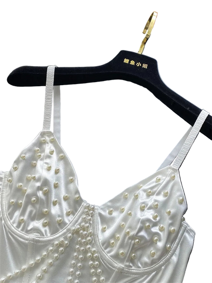 White lace top with pearl embellishments on a black hanger against a white curtain background.