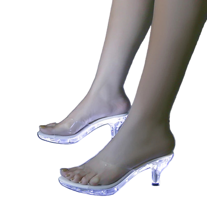 Clear high-heeled shoes with LED lights on a reflective surface