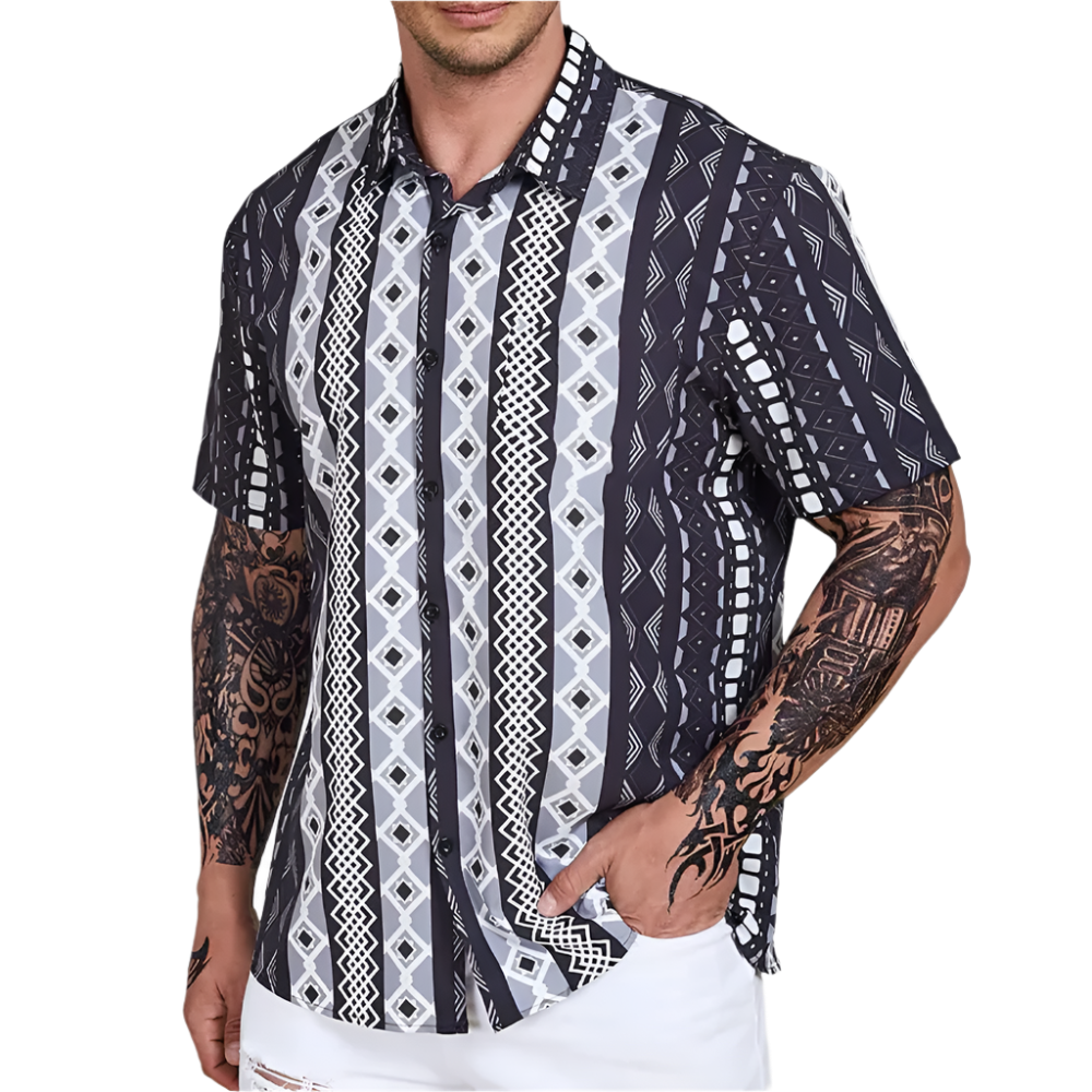 Man wearing a patterned shirt with tattoos on arms against a gray background