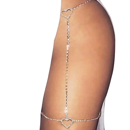 A close-up of a model's upper thigh wearing a delicate silver chain garter-style accessory with two heart-shaped links, one near the hip and one on the upper thigh.