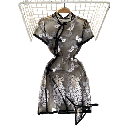 Black embroidered dress on a hanger with white flowers and a hat in the background