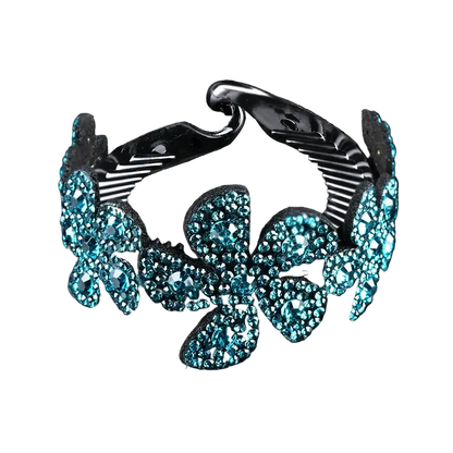 A silver-toned metal cuff bracelet decorated with large, glittering turquoise blue flower-shaped crystals, shown against a solid black background with a subtle reflection.
