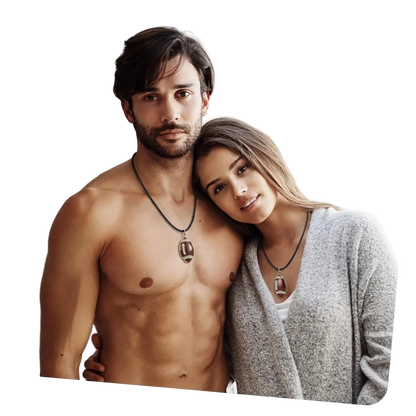 A shirtless man and a woman wearing matching pendant necklaces with football-shaped charms, posed closely together in an indoor setting.
