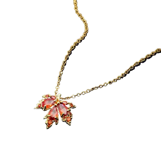 Gold necklace with a leaf-shaped pendant featuring red and pink gemstones on a dark background.