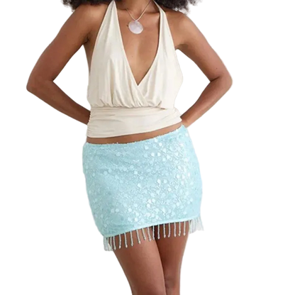 A woman modeling a light blue sequined mini skirt with fringe trim and a cream halter top against a plain white background.