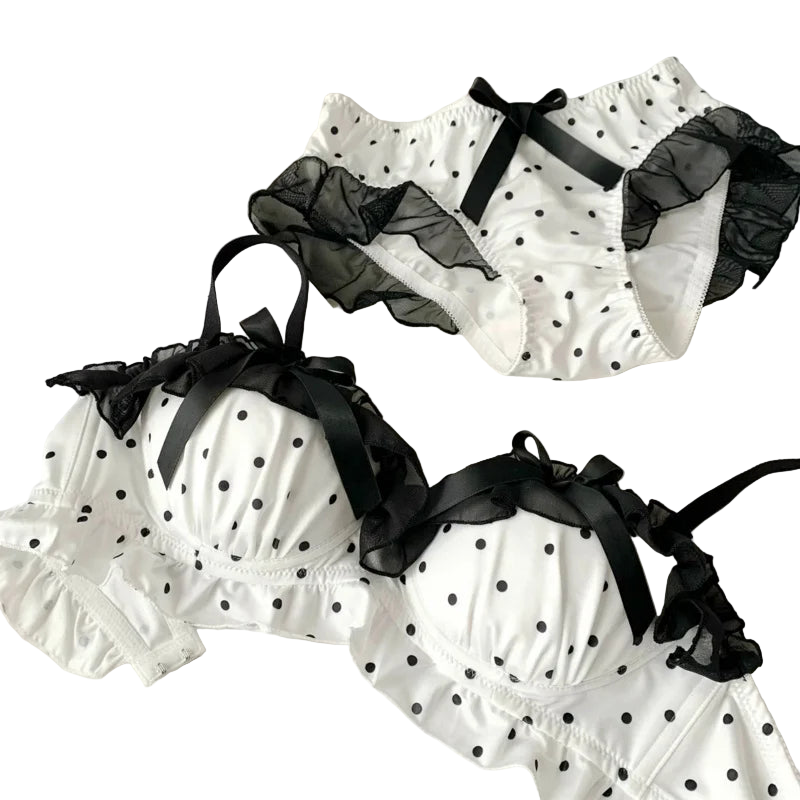 White polka dot lingerie set with black ribbons on a white surface.