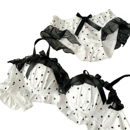 White polka dot lingerie set with black ribbons on a white surface.