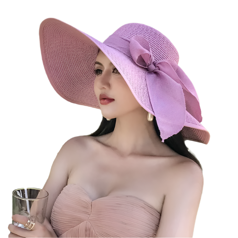 Woman wearing a pink sun hat with a bow, sitting outdoors among green plants.